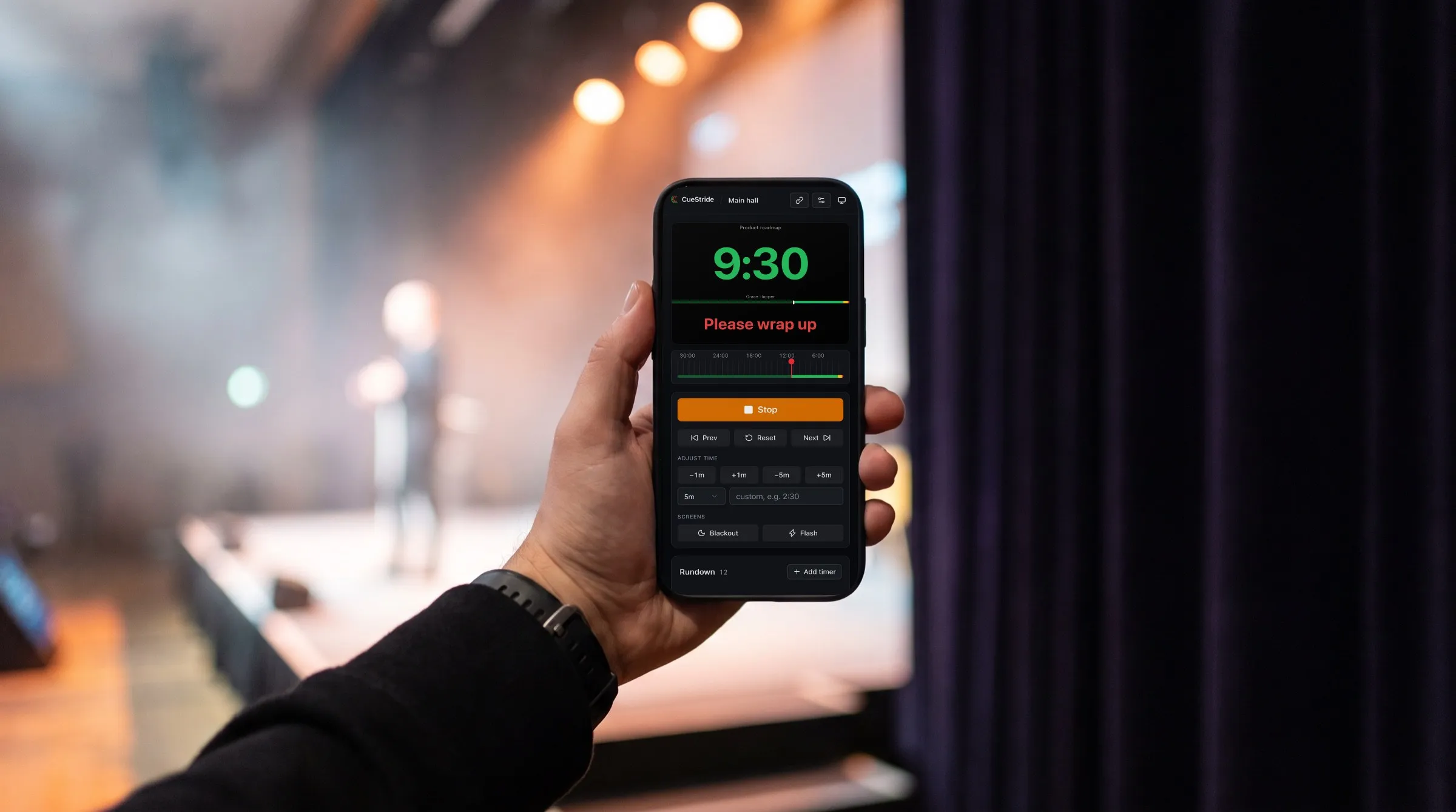 Illustration of a producer's hand holding a phone beside a stage: the phone shows CueStride's real controller at 9:30 with Please wrap up on the stage preview.